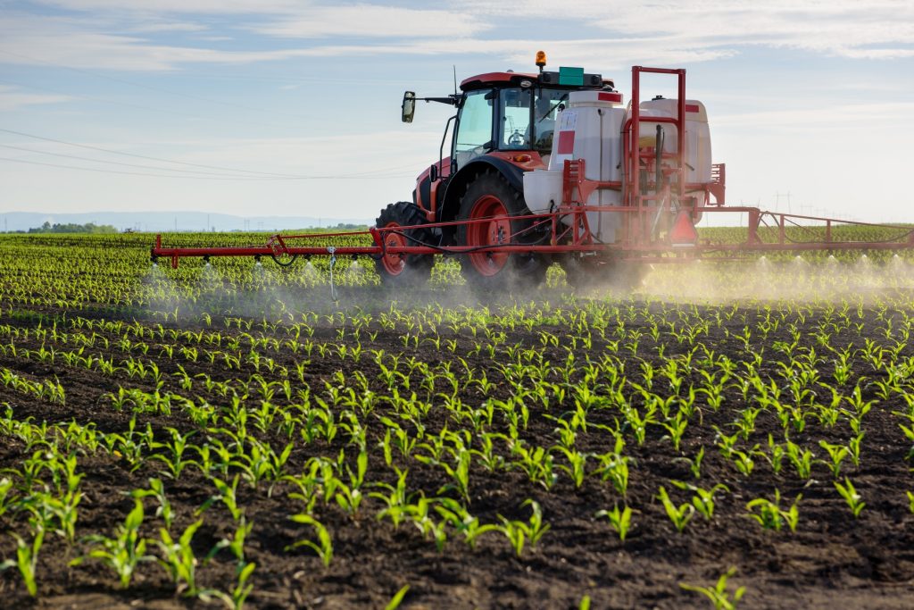 A red tractor sprays row crops.